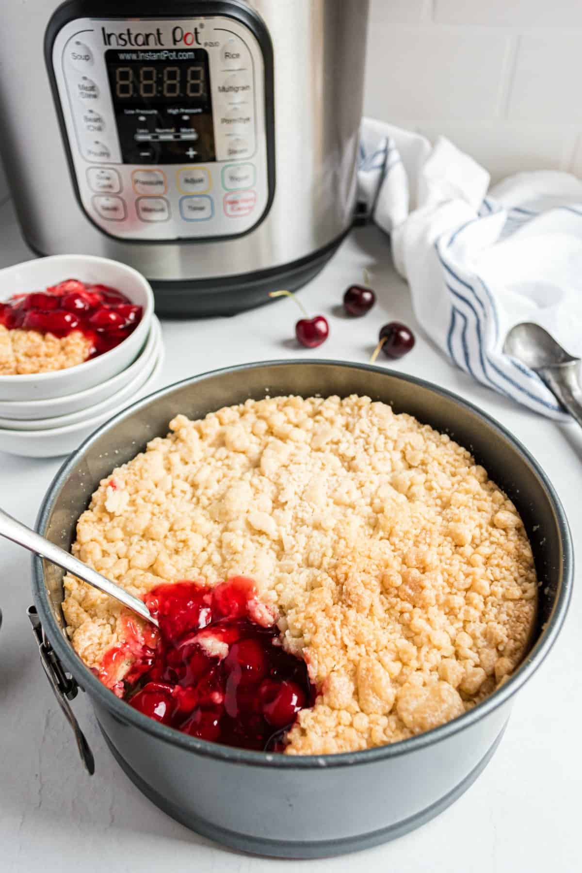 Cherry cobbler in a springform pan with one scoop missing and instant pot in background.