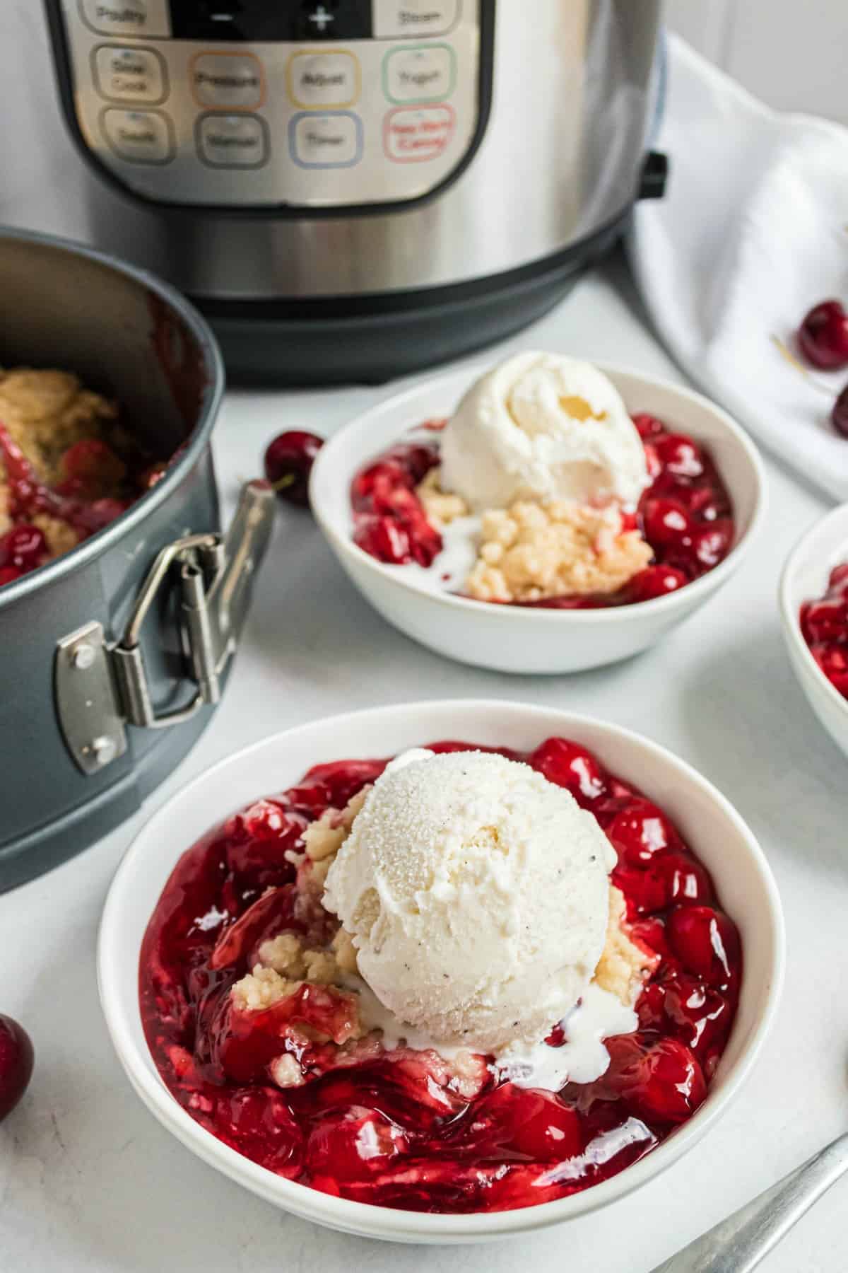 Cherry cobbler topped with vanilla ice cream in a white bowl.