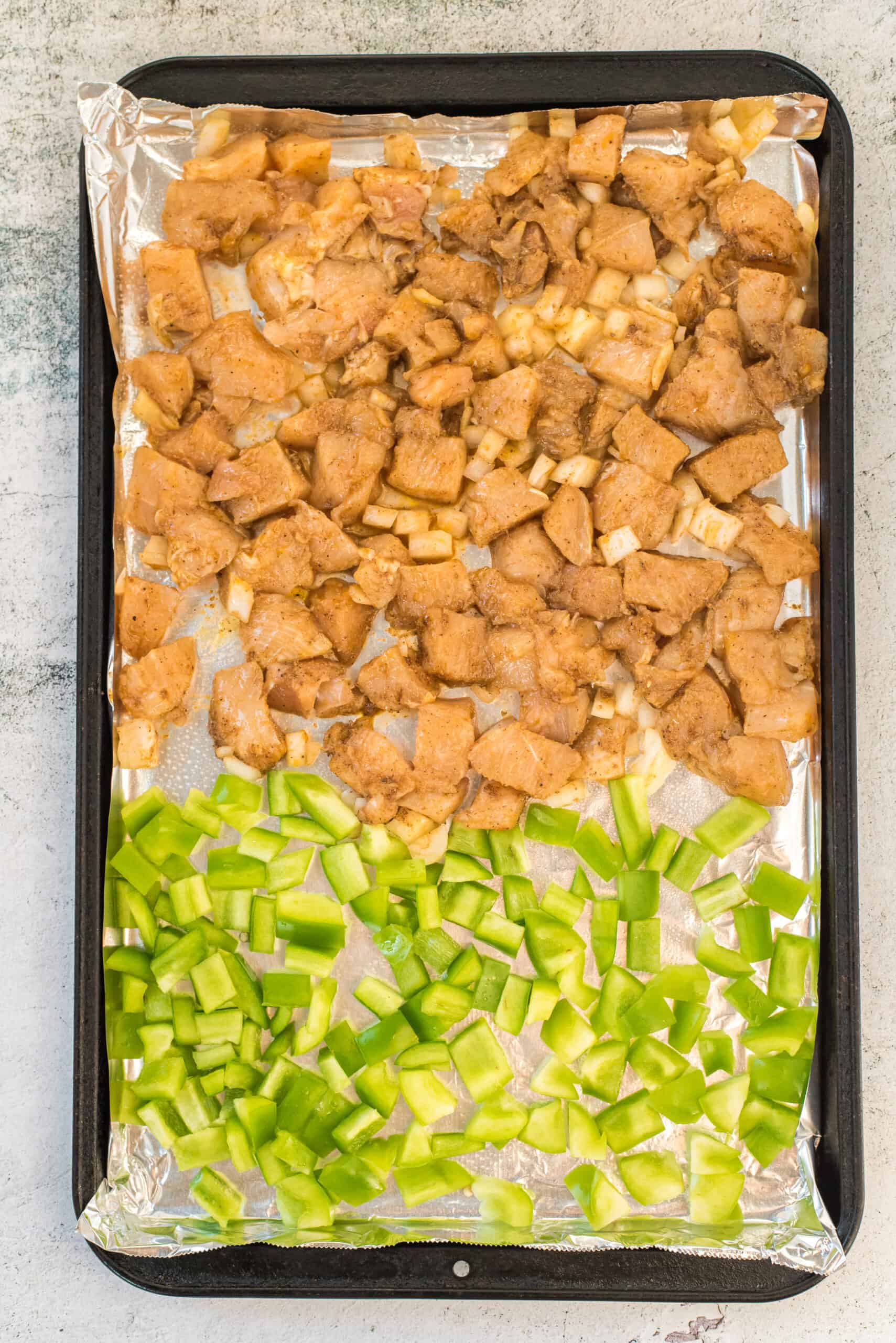 Baking sheet with chicken, onion, and peppers.