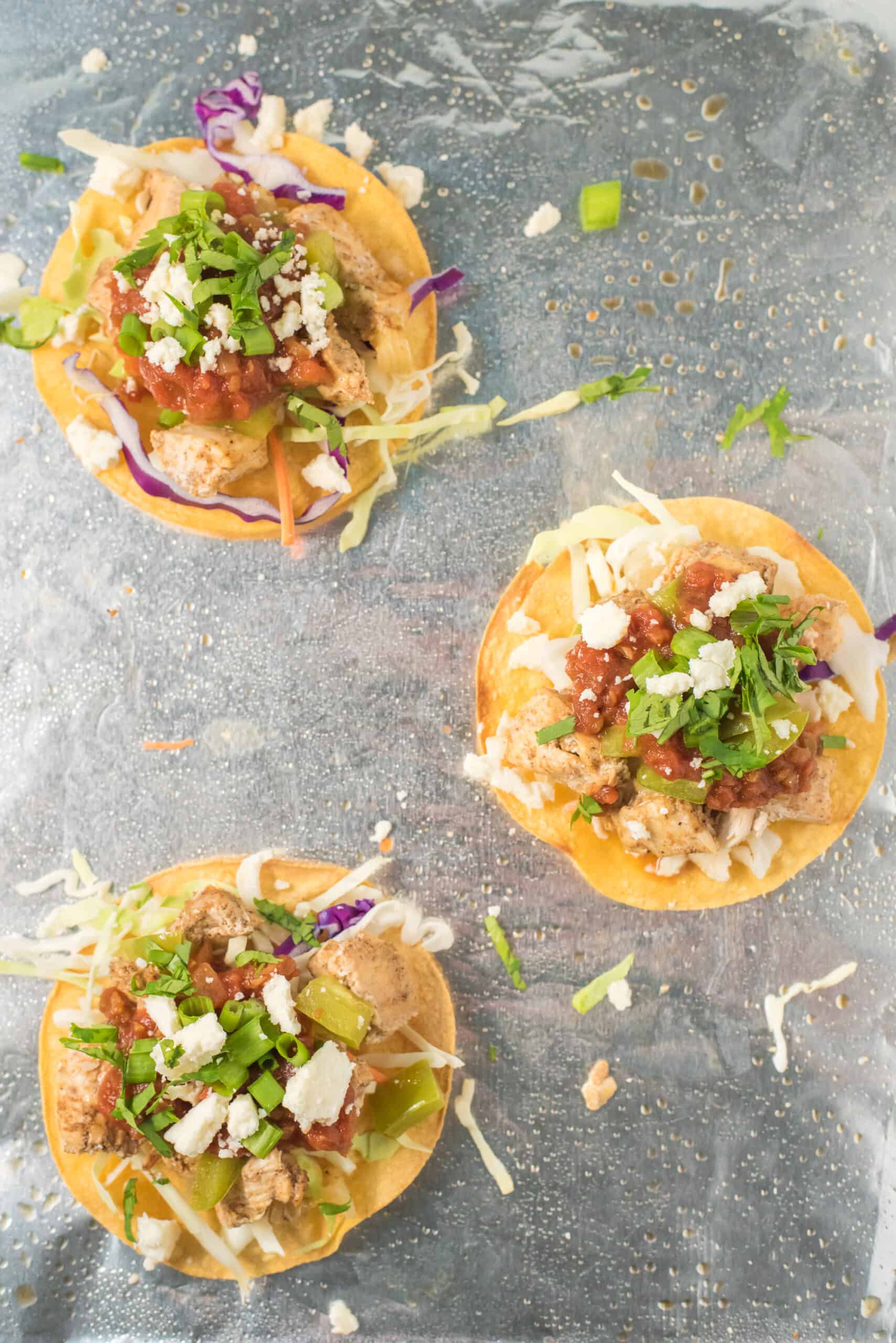 Three chicken tostadas on a foil lined baking sheet.