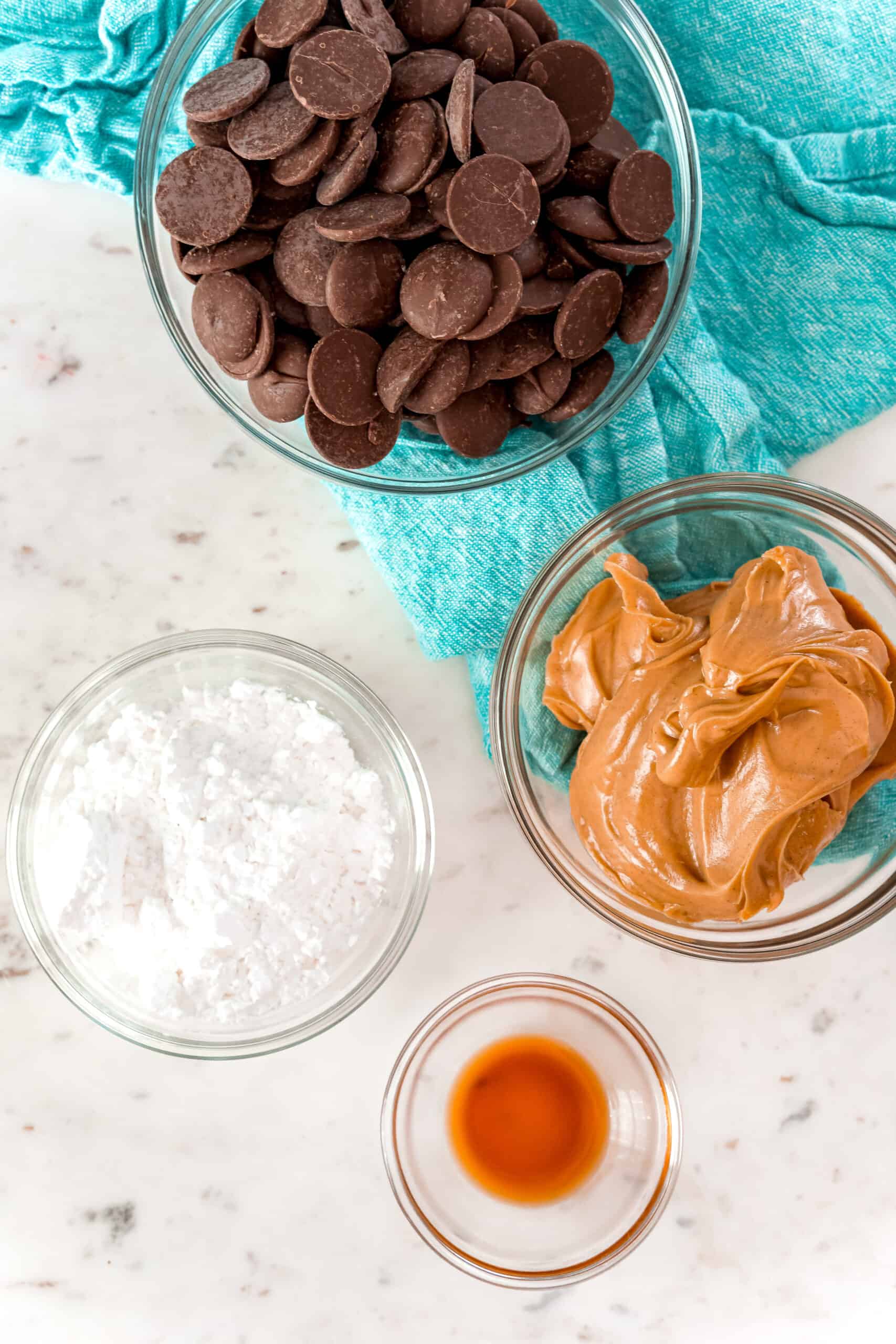 Four ingredients to make homemade peanut butter cups including chocolate, sugar, vanilla, and peanut butter.