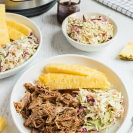 Pulled pork on a plate with pineapple and coleslaw. Pressure cooker in background.