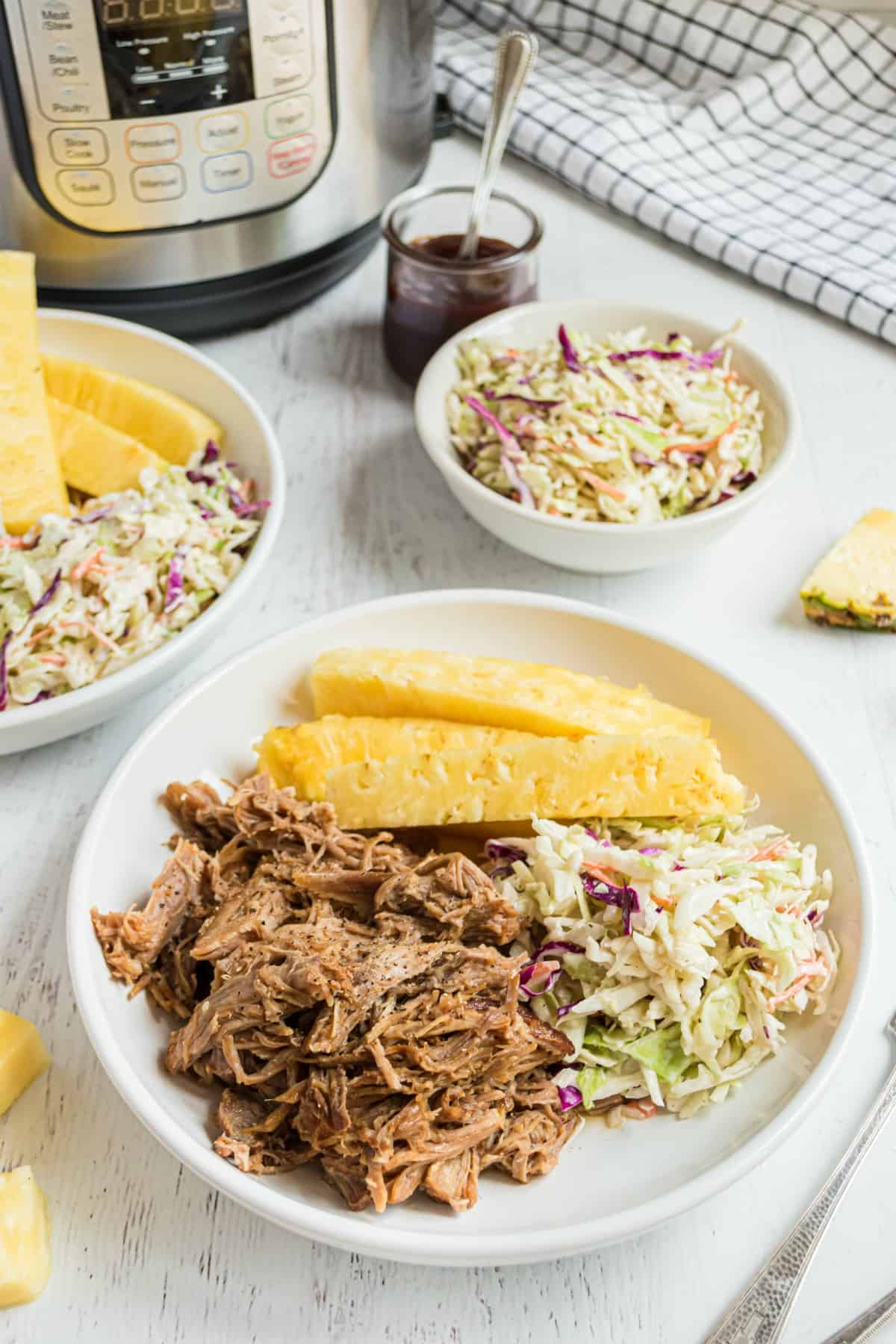 Pulled pork on a plate with pineapple and coleslaw. Pressure cooker in background.