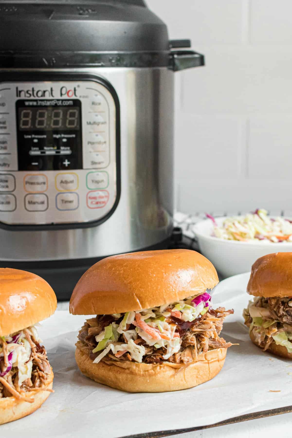 Instant Pot Hawaiian Pork sandwiches on a white plate with pressure cooker in background.