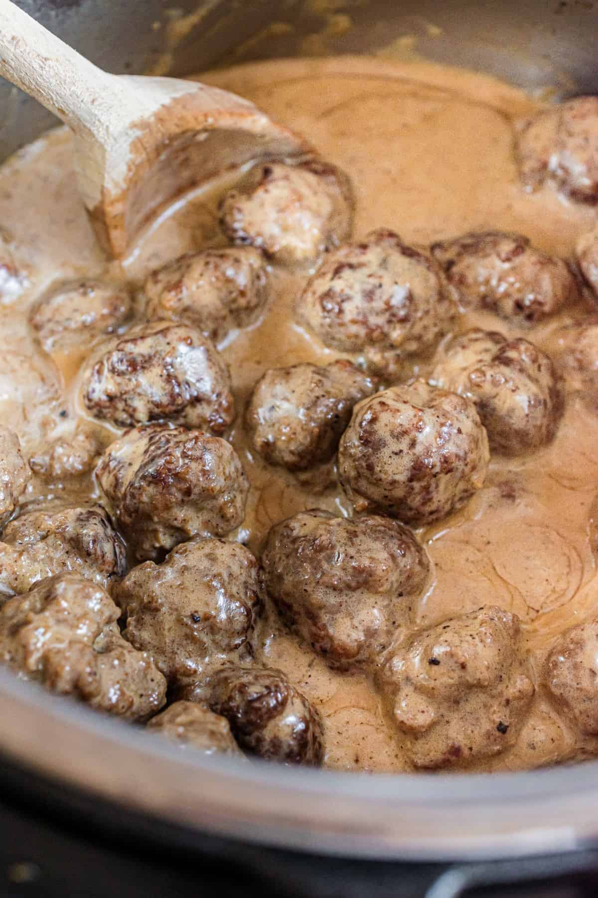 Swedish meatballs in the pressure cooker being stirred with a wooden spoon.