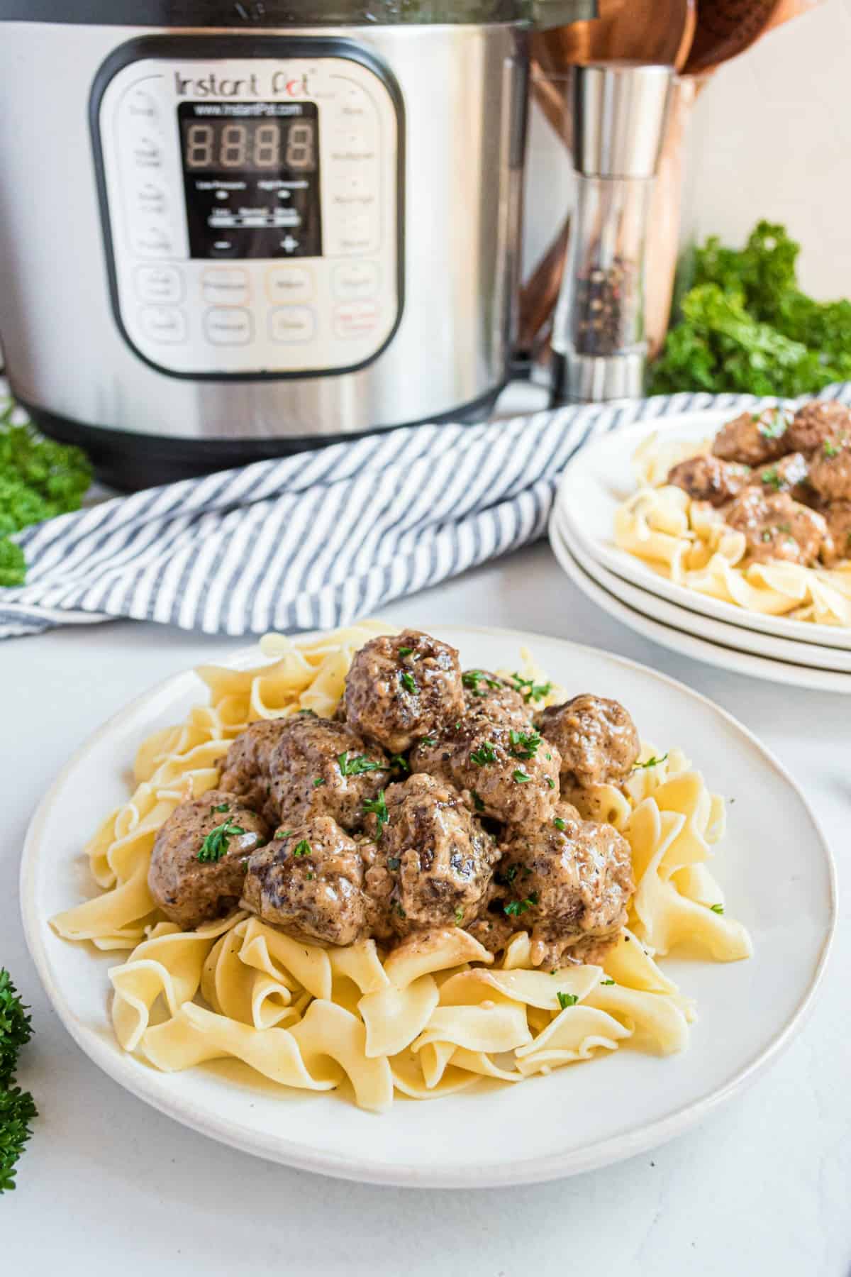 Swedish meatballs served on a plate of egg noodles with instant pot in background.