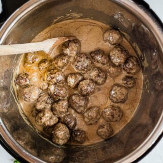 Swedish meatballs in the instant pot being stirred with a wooden spoon.
