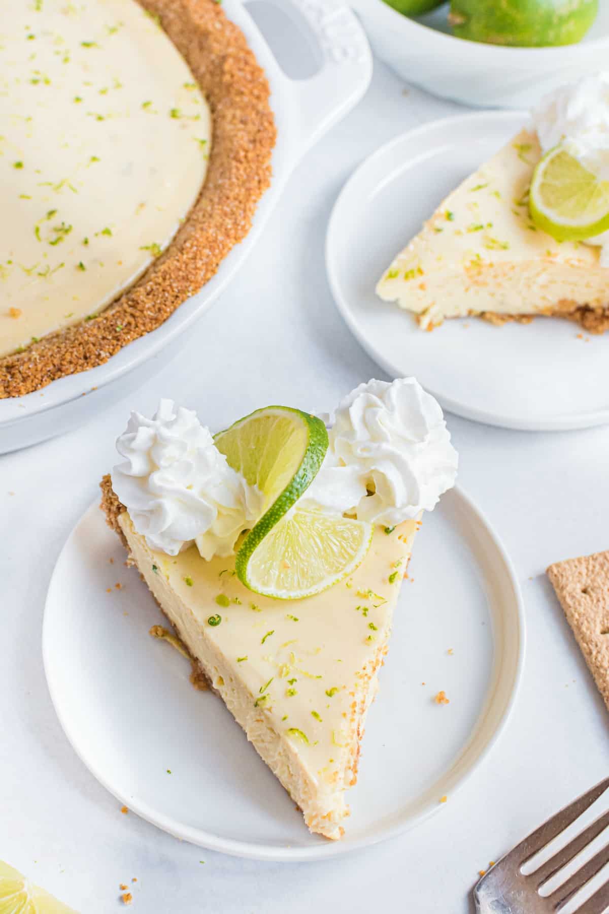 Slice of key lime pie with whipped cream on a white plate.