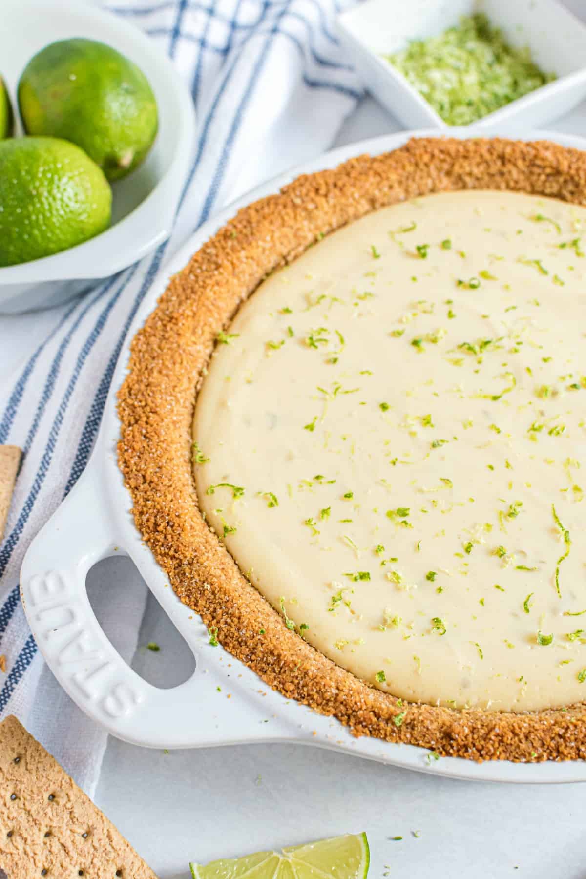 Key lime pie in a white pie plate garnished with lime zest.