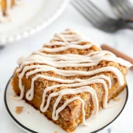 Pumpkin cake with cinnamon crumb and cream cheese frosting on a white dessert plate.