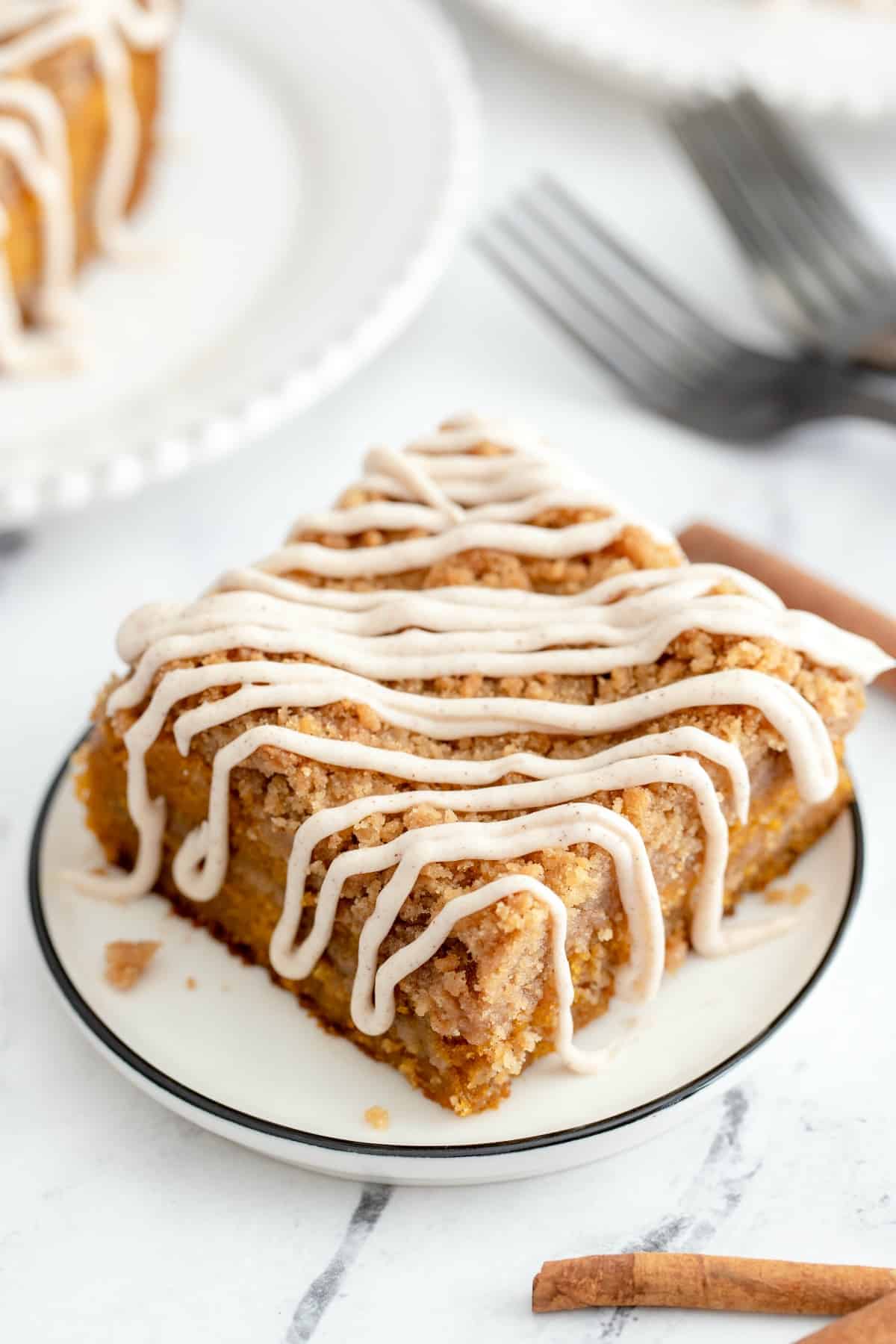 Pumpkin cake with cinnamon crumb and cream cheese frosting on a white dessert plate.