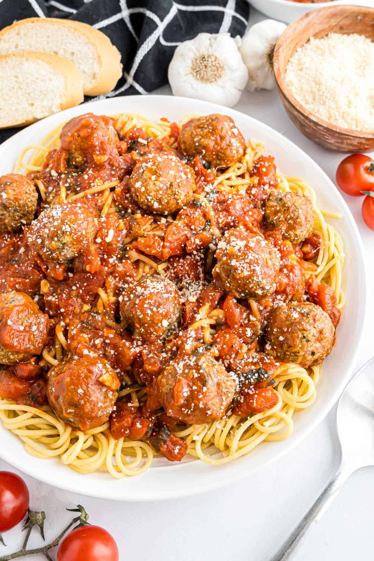 A plate of spaghetti topped with turkey meatballs with bruschetta sauce, sprinkled with cheese, served alongside fresh bread and ripe tomatoes.