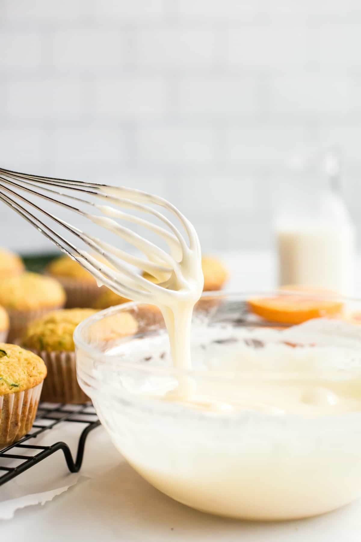 Orange glaze in a glass bowl with whisk for zucchini muffins.