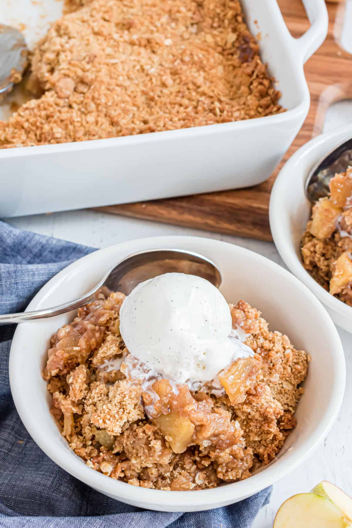 Apple crumble scooped into a white bowl and topped with vanilla ice cream.