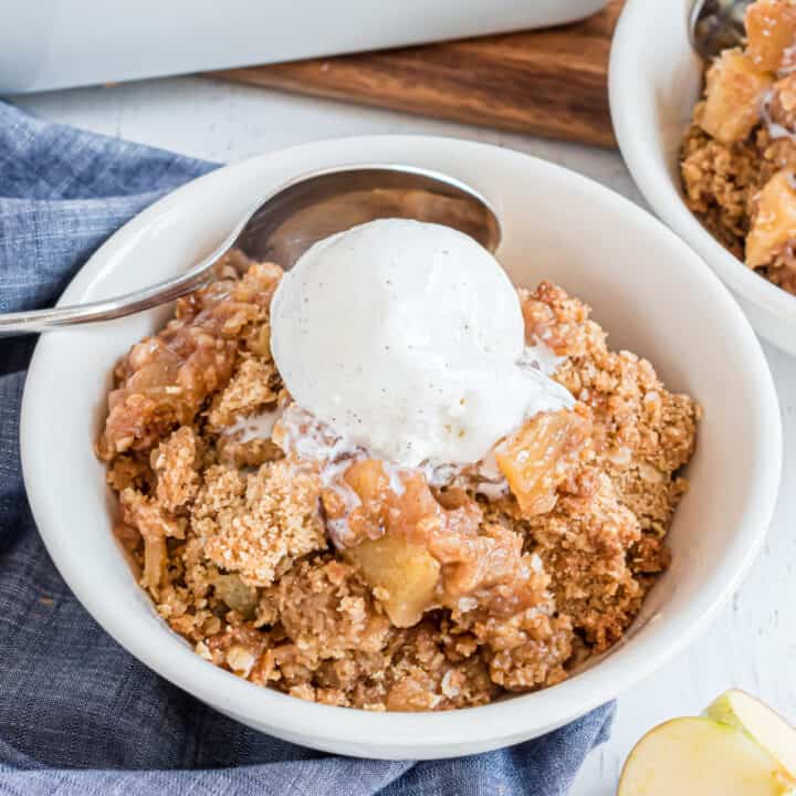 Apple crumble in a bowl with vanilla ice cream on top.