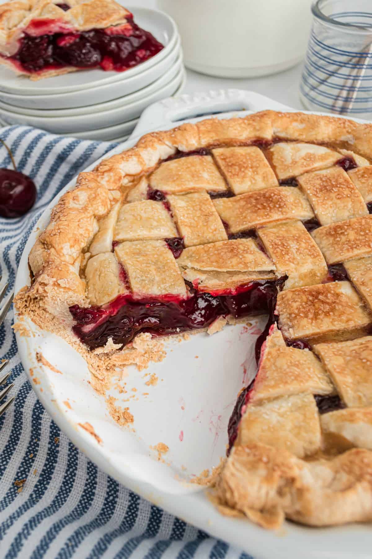 Whole cherry pie in a white pie plate with one slice removed.