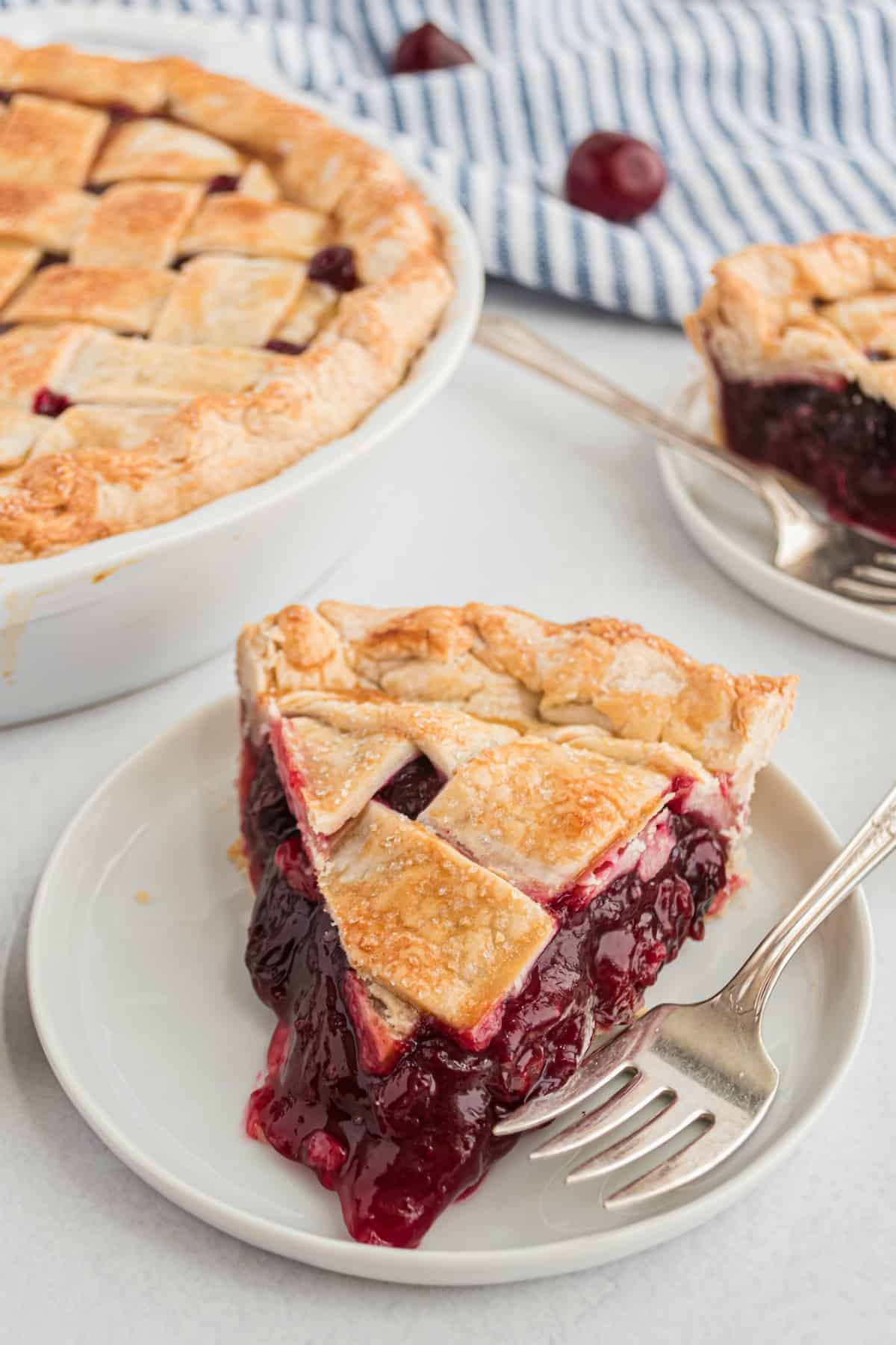 Slice of cherry pie with lattice crust on a white plate.