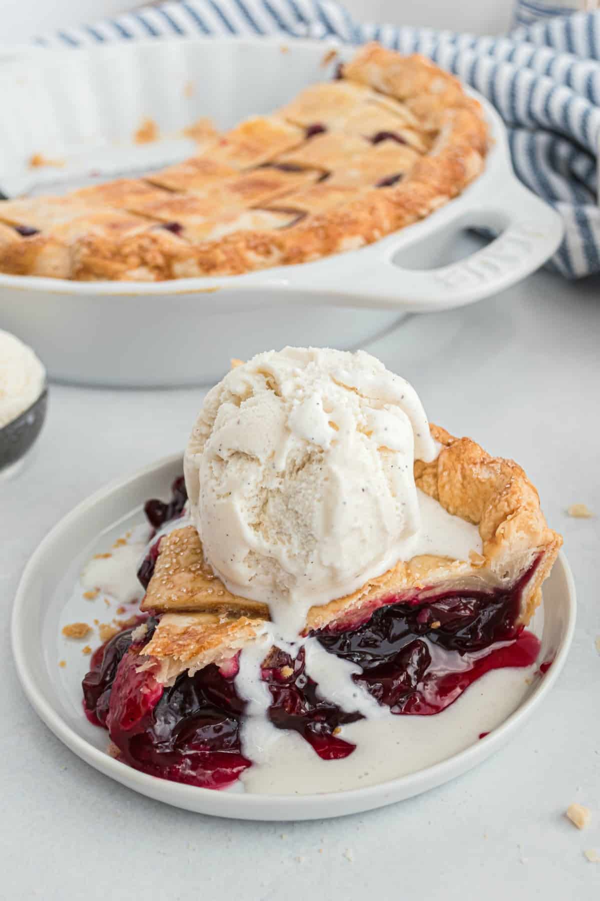 Slice of cherry pie with a scoop of vanilla ice cream melting on top.