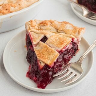 Slice of cherry pie with lattice top on a white plate.