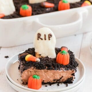 Slice of halloween dirt cake on a white plate, decorated with tombstone cookie and candy corn.