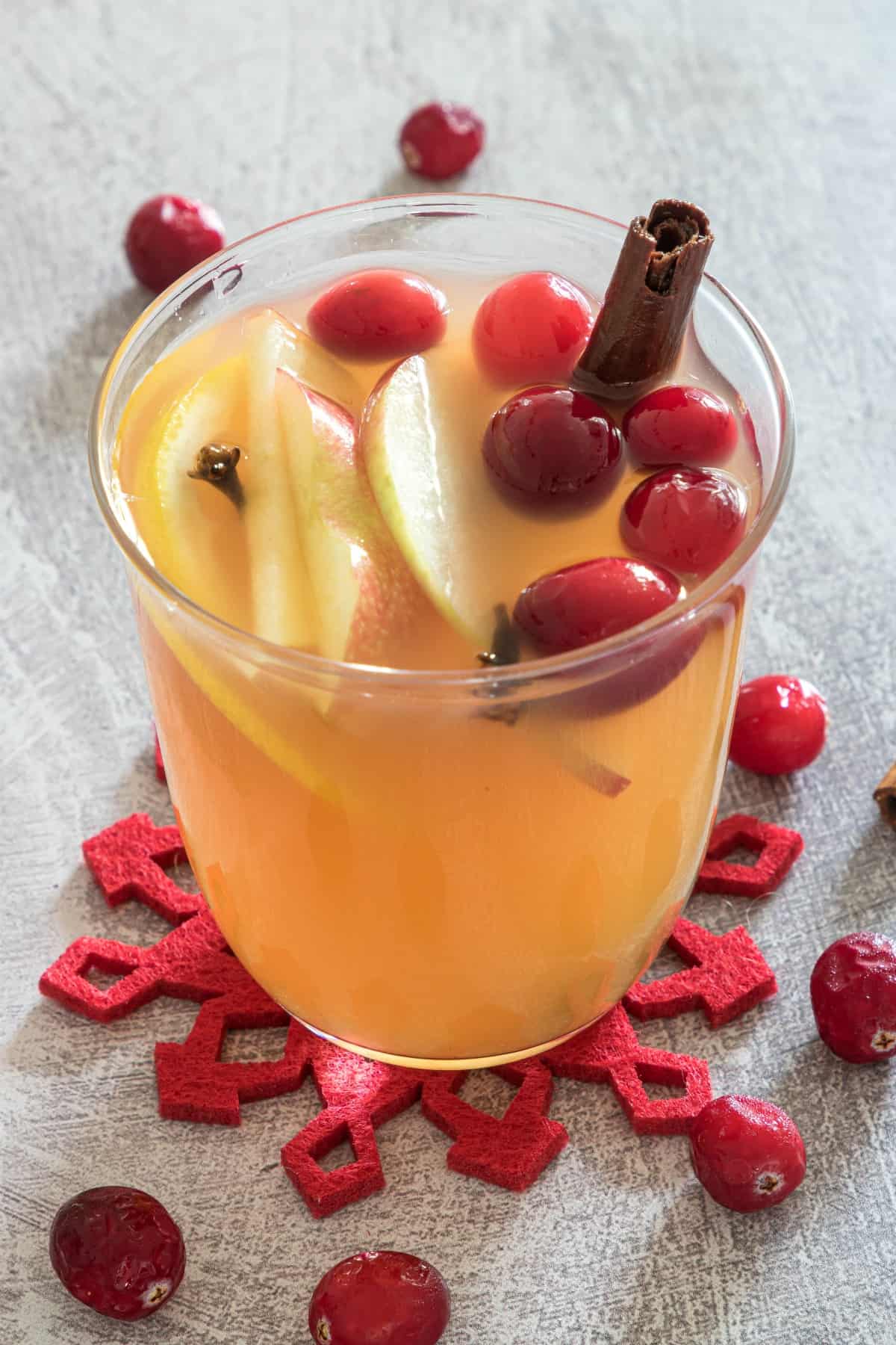 Clear glass with homemade apple cider, apples, cranberries, and a cinnamon stick.