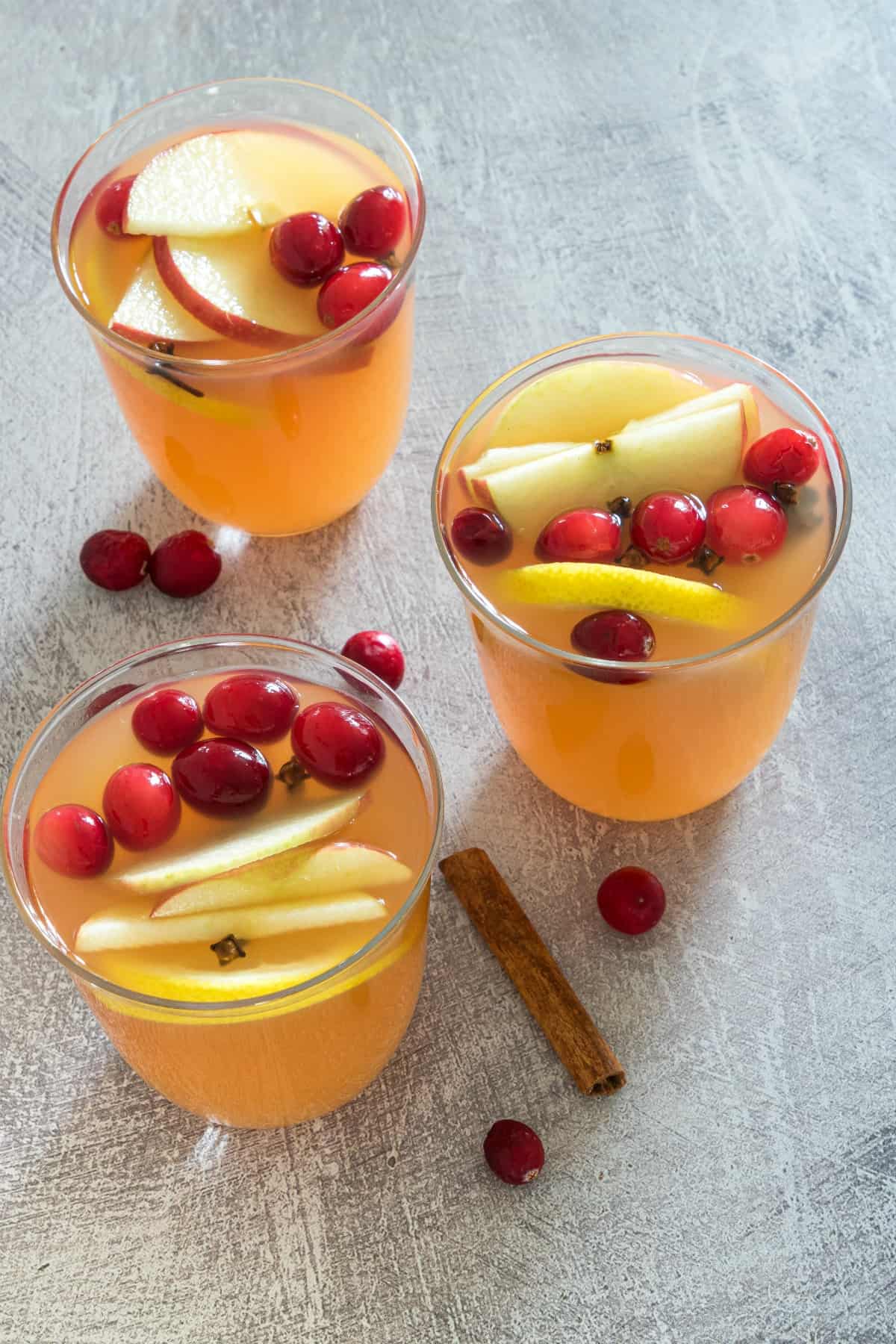 3 cups of apple cider in clear glasses, garnished with cranberries and apple slices.