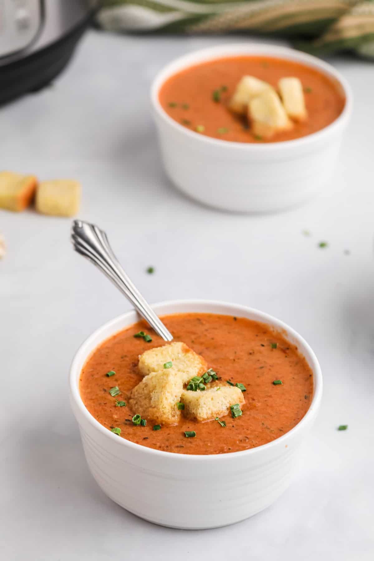 Two small white bowls of tomato soup with croutons.