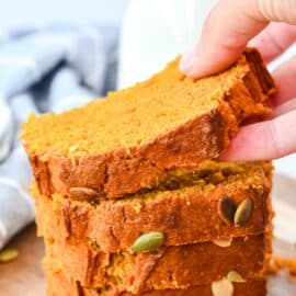 Stack of sliced pumpkin bread with one piece being lifted off stack.