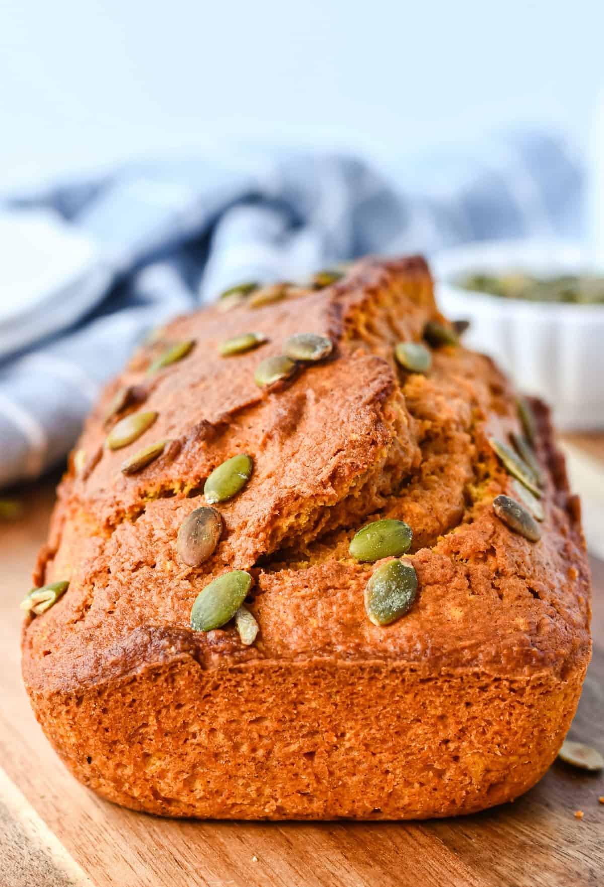 Loaf of pumpkin bread with pumpkin seeds on wooden cutting board.