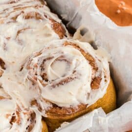 Pumpkin cinnamon rolls in parchment paper lined baking dish with maple icing.
