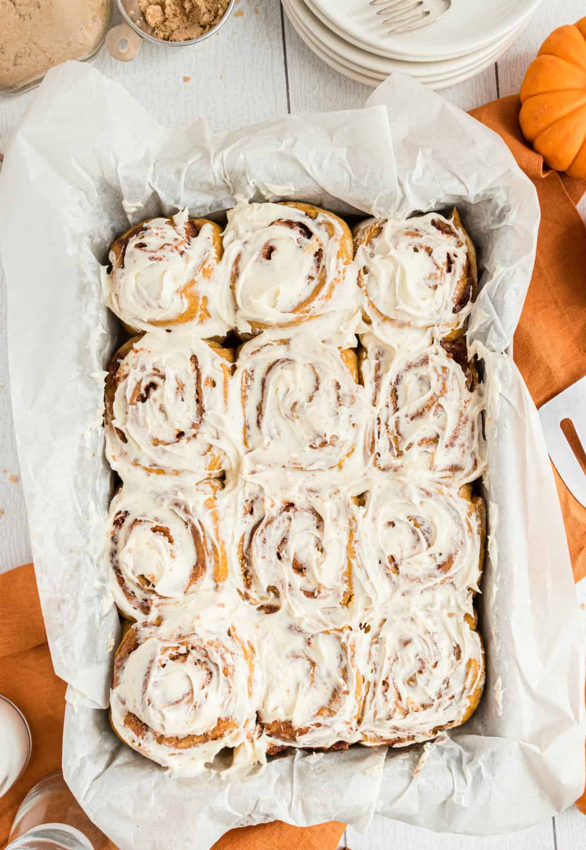 Pumpkin cinnamon rolls with maple icing in a parchment paper lined 13x9 baking dish.