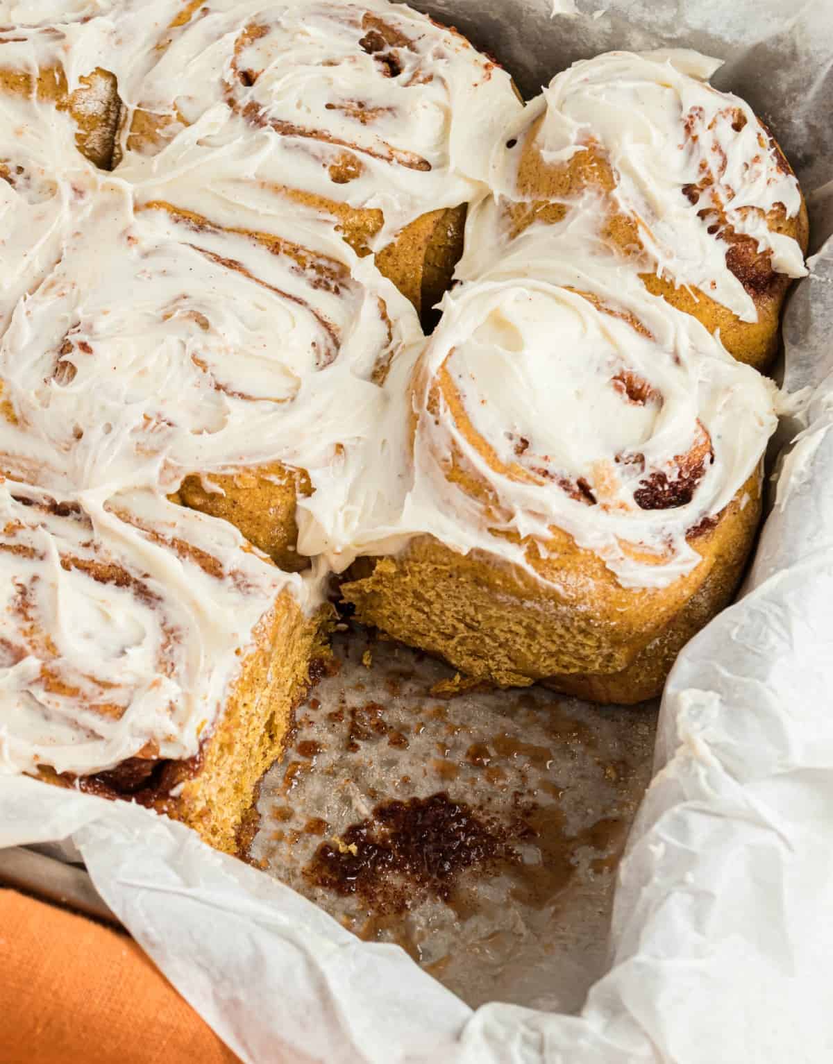 Pumpkin cinnamon rolls in 13x9 baking dish with one roll removed.