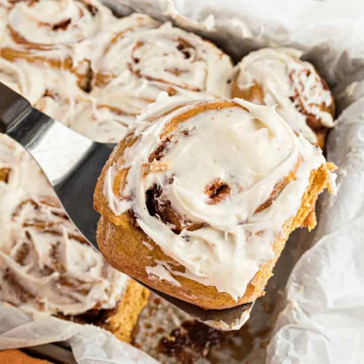 Pumpkin cinnamon roll being lifted out of the pan with a spatula.