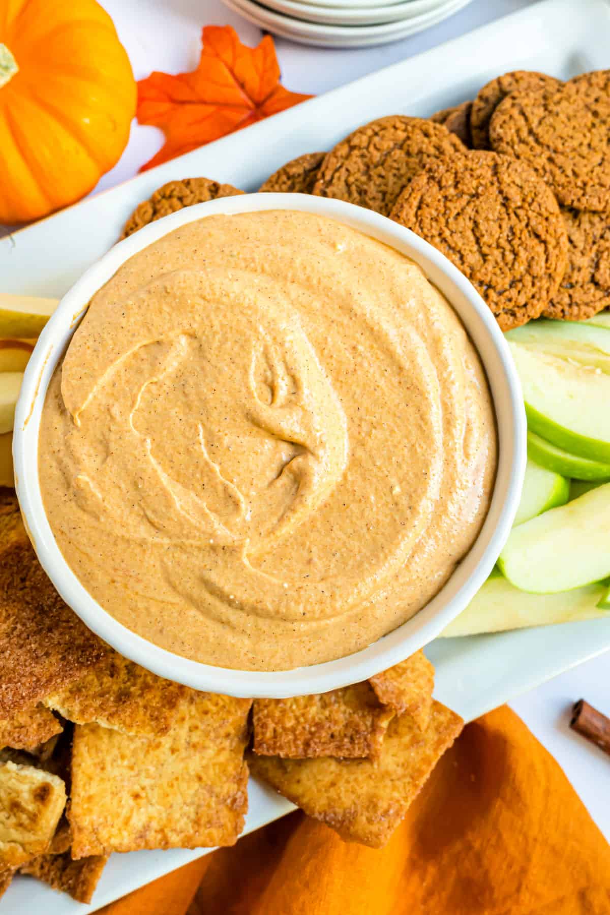 Pumpkin pie dip in a white bowl with cookie and apple dippers on side.