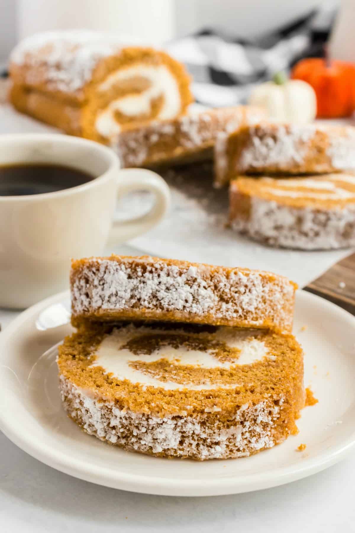 Two pumpkin roll slices on a white plate, with remaining cake in background.