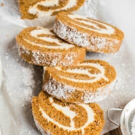 Pumpkin roll slices fanned out on parchment paper, with cream cheese frosting.
