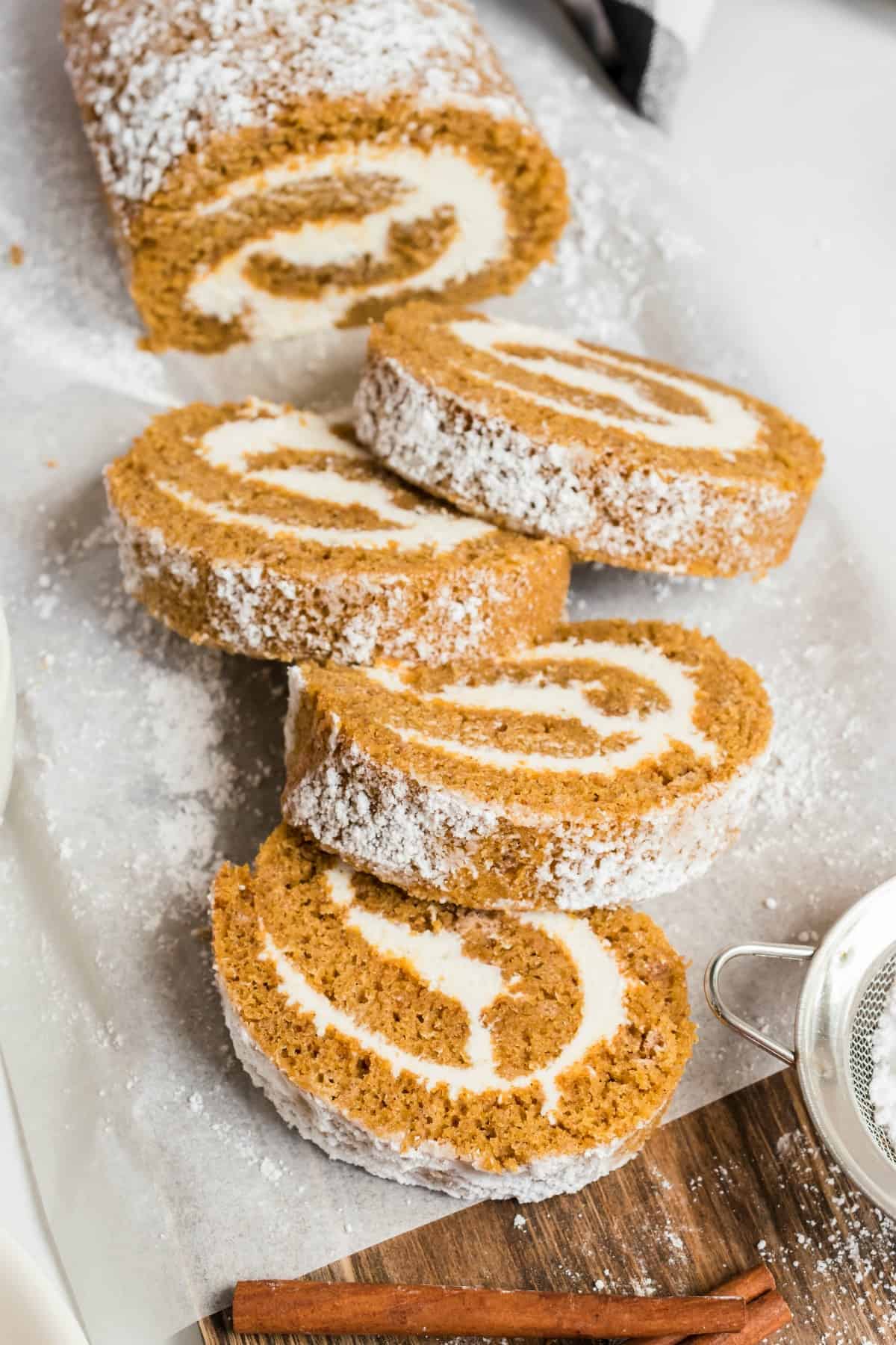 Pumpkin roll slices fanned out on parchment paper, with cream cheese frosting.