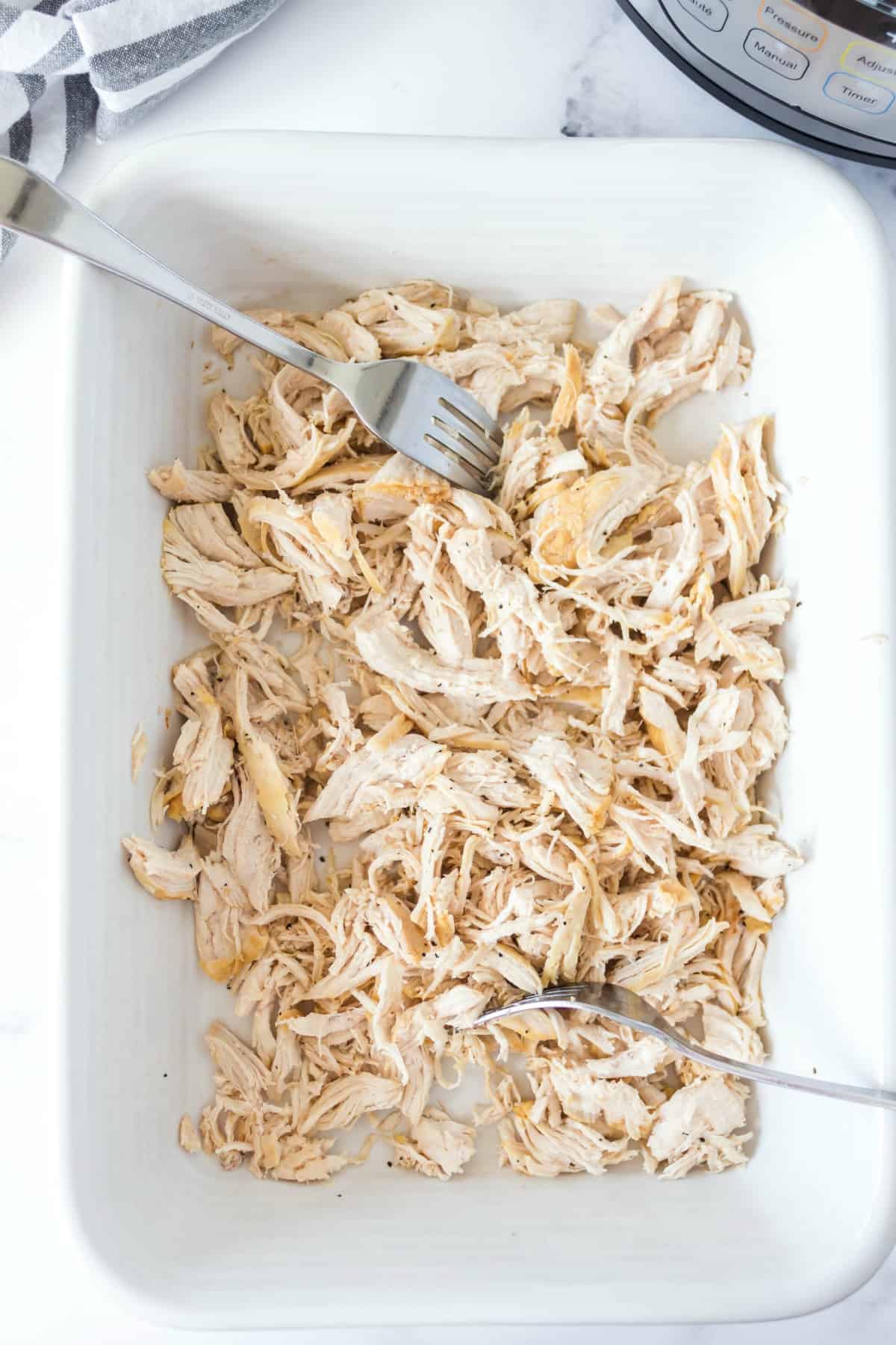 Shredded chicken in a white baking dish with fork.