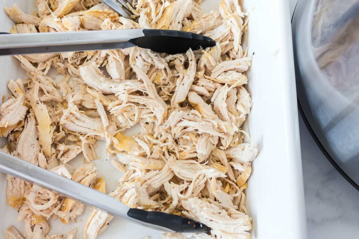 Shredded chicken in a white dish with tongs.