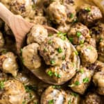 A wooden spoon scooping Swedish meatballs in creamy gravy garnished with parsley.