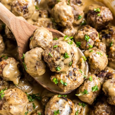 A wooden spoon scooping Swedish meatballs in creamy gravy garnished with parsley.