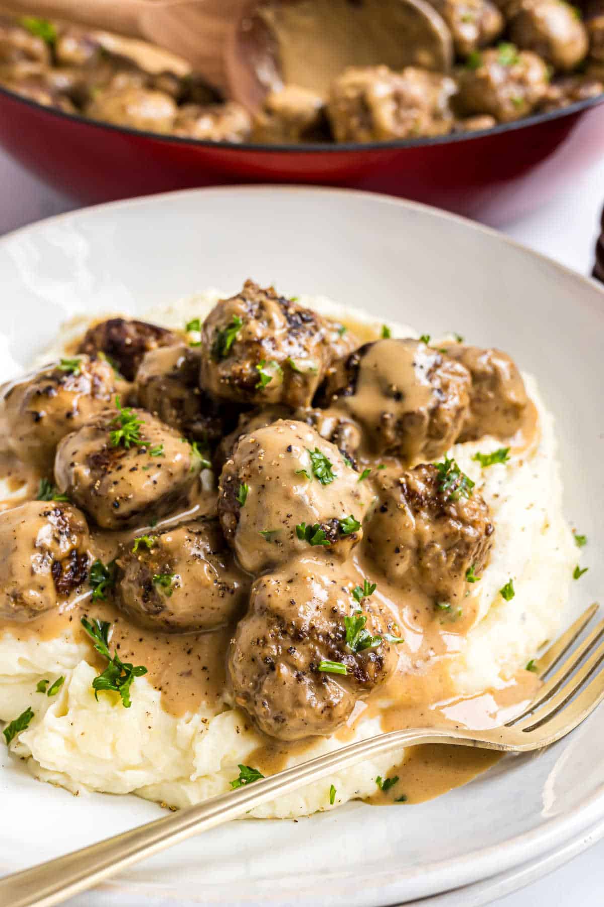Swedish meatballs served in gravy over mashed potatoes, garnished with parsley.