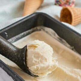 Homemade vanilla ice cream in metal loaf pan with ice cream scoop.