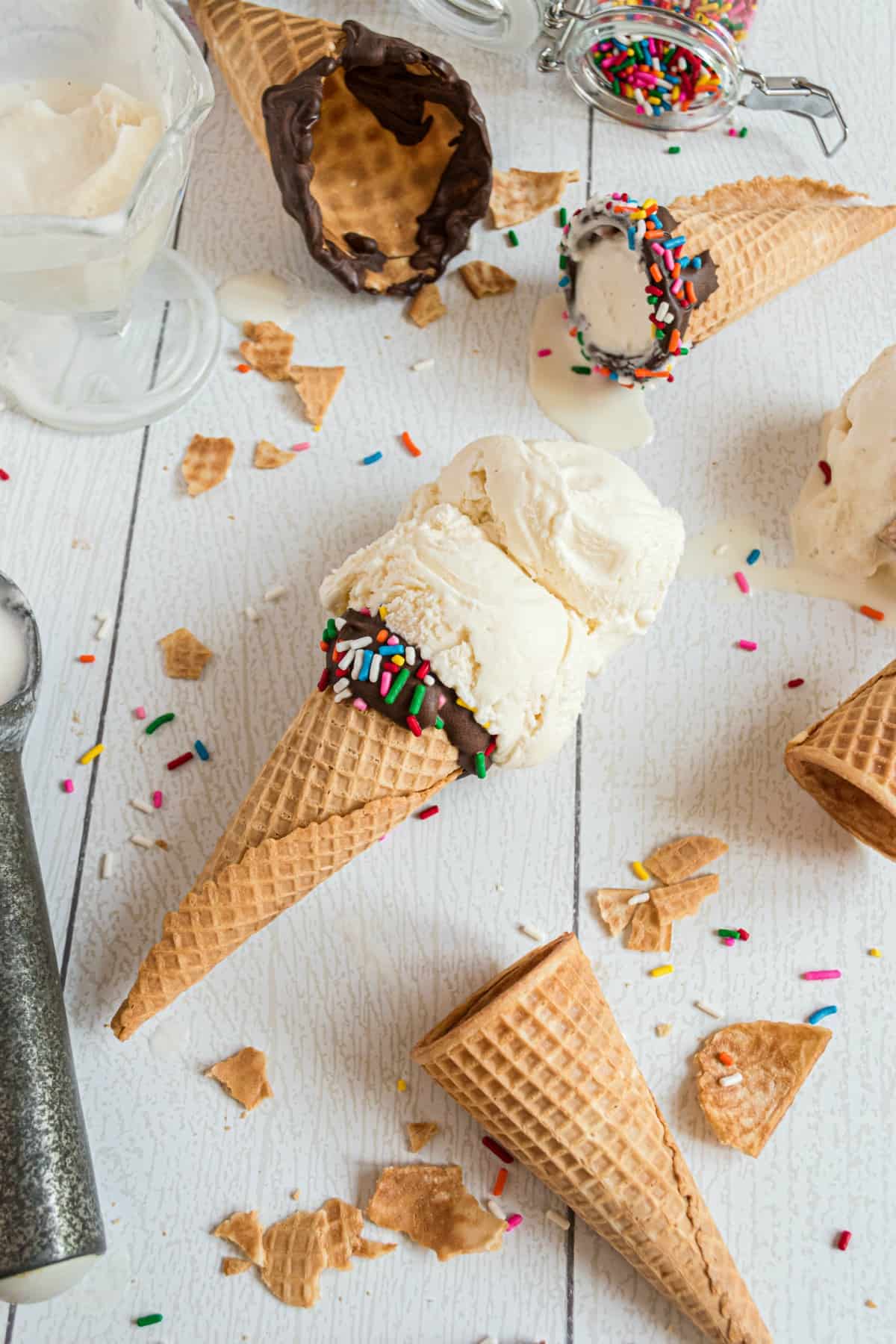 Vanilla ice cream on a sugar cone with cracked cones in background.