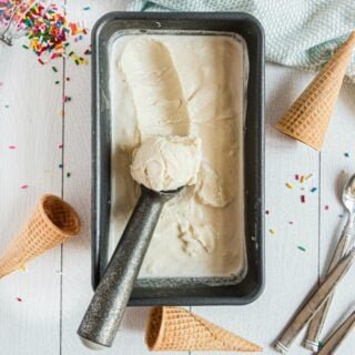 Homemade vanilla ice cream in metal loaf pan with ice cream scoop.