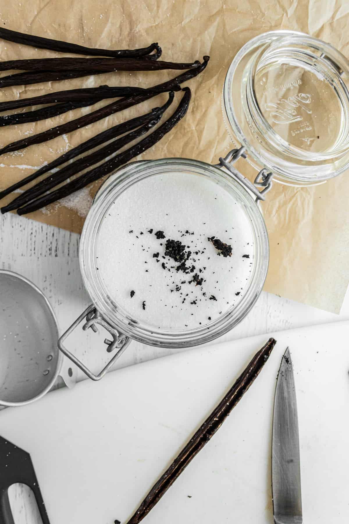 Sliced vanilla bean with seeds removed and in a jar of sugar.