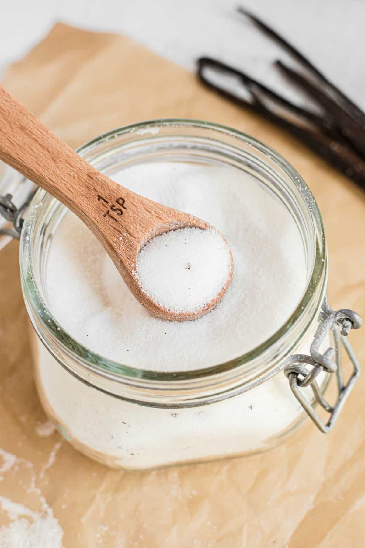 Homemade vanilla sugar in a mason jar with teaspoon scoop.