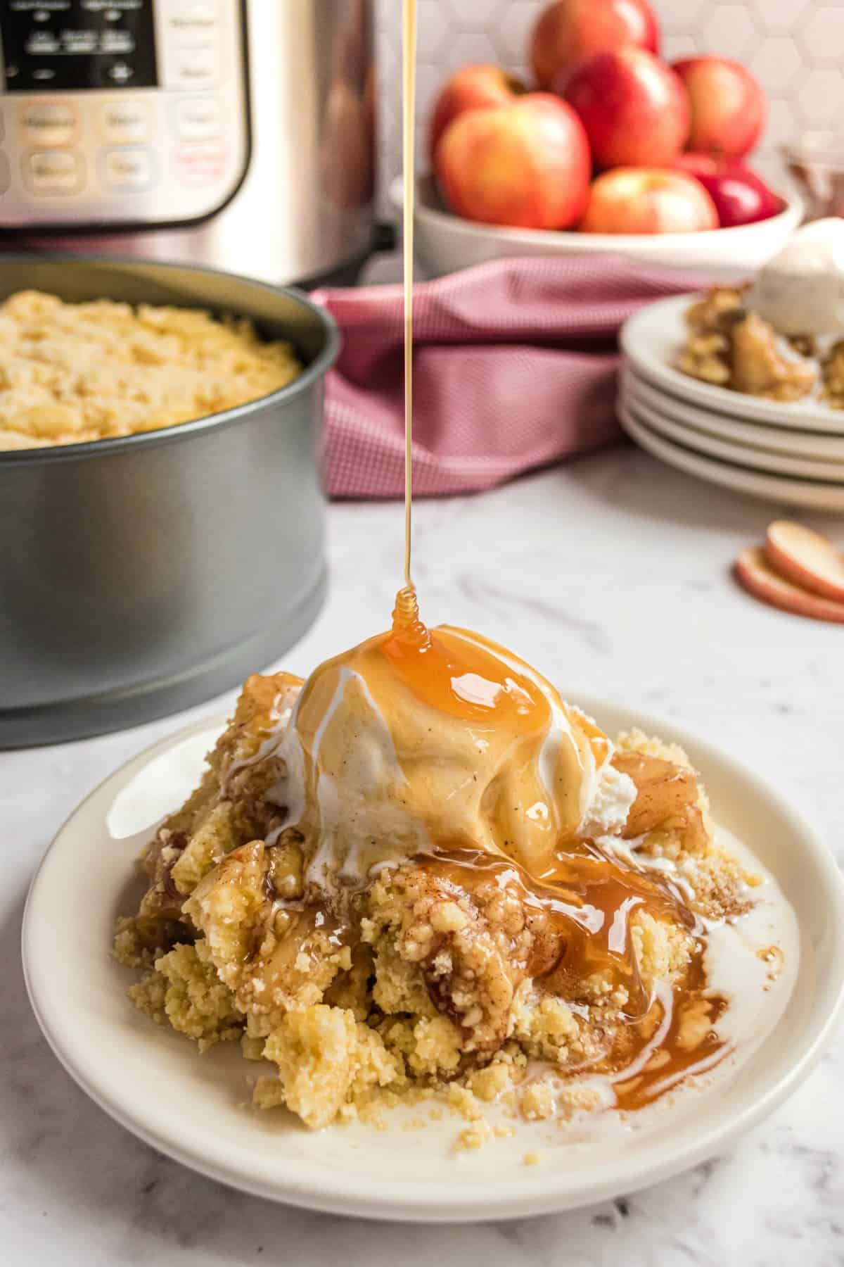 Apple cobbler on a plate with caramel sauce and ice cream.