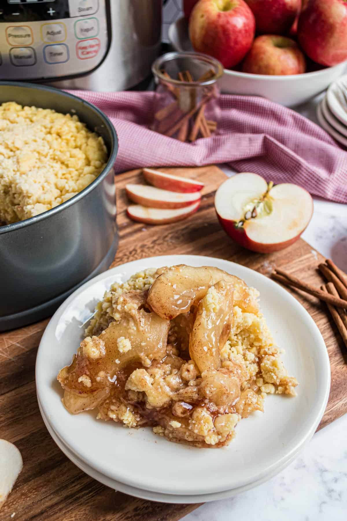 Apple cobbler on white dessert plate with instant pot in background.