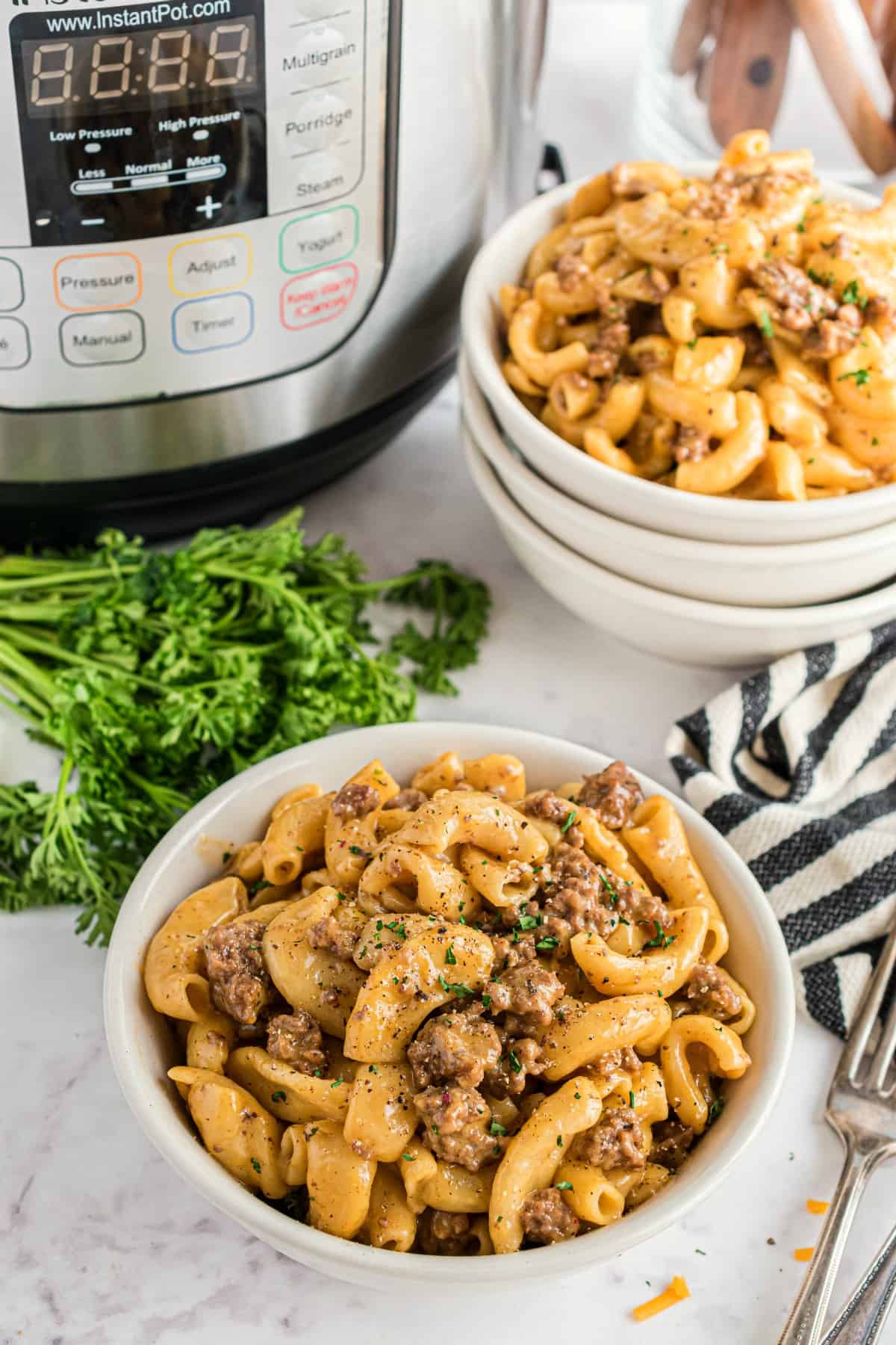 Two white bowls with hamburger helper with parsley and Instant Pot in background.